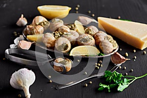 Selective focus of delicious cooked escargots with lemon slices near cutlery, black peppercorn and Parmesan on black