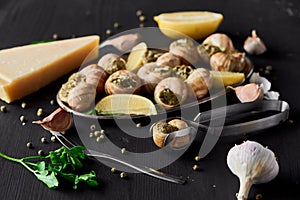 Selective focus of delicious cooked escargots with lemon slices near garlic, cutlery, black peppercorn and Parmesan on