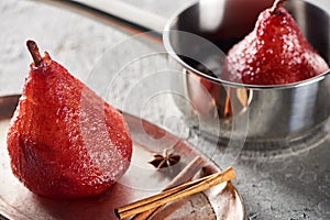 Selective focus of delicious pear in wine in stewpan and on silver plate with cinnamon and anise on grey concrete surface