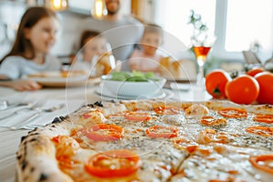 Selective focus of delicious pizza with tomatoes on wooden table with blurred family in background
