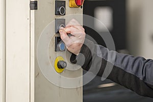 Selective focus. Detailed view of an arm and hand from a blue-collar working pushing on a button from a hydrolic car lift.