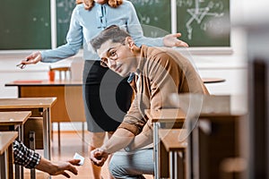 Selective focus of dissatisfied female teacher looking at male student taking crib during exam