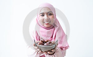 Selective focus on dry dates fruit in bowl. Asian 30s Muslim woman wearing traditional clothes with hijab, smiling holding energy