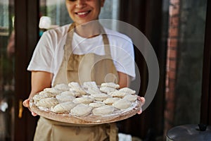 Selective focus on dumplings or vareniki on a wooden board in the hands of a charming woman housewife in chef's