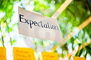 Selective focus on expectation word hand writing on white paper stick on the glass with natural sunlight and green leave in the