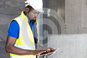 Selective focus at face of Black African foreman at building construction site, wearing protective hat and safety equipment while