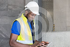 Selective focus at face of Black African foreman at building construction site, wearing protective hat and safety equipment while