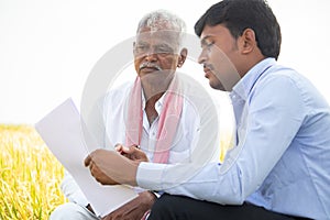 Selective focus on farmer, Bank officer explaning about farm loan paper documents to Indian farmer near agriculture field -