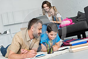 selective focus of father and son doing homework together while mother and daughter using laptop on sofa