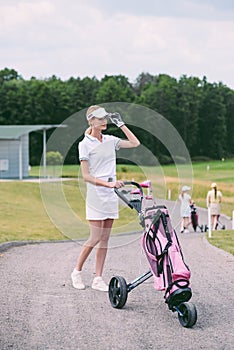 selective focus of female golf player in cap and white polo with golf gear
