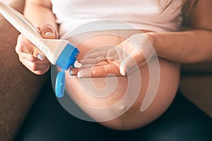 Pregnant female keeping cream and applying it on big belly