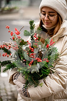 selective focus on flower arrangement in pot of spruce branches and red berries and eucalyptus in female hands