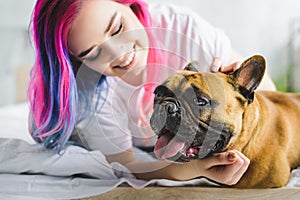 Selective focus of girl with colorful hair petting and looking at cute french bulldog while laying