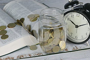 Selective focus of Gold coins on book with clock. Finance and education concept