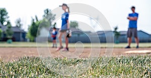 Selective focus on grass with blurred girls softball game in the background