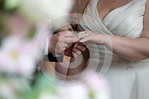 Selective focus of the groom putting the wedding ring on the finger of the bride in a white dress