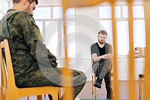 Selective focus of group male soldiers in camouflage uniform talking sitting in circle during PTSD group therapy session