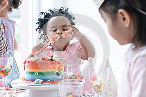 Selective focus on hand of African little child girl holding jelly, enjoy eating rainbow cake on birthday party with fork. Kids