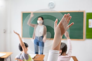 Selective focus on hand. Children or Schoolkids or students raising hands up with Asian teacher wearing protective face mask in photo