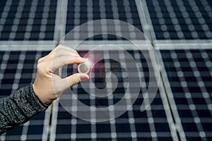 Selective focus on hand holding 1 euro coin and blurred solar panel cell on background with copy space.