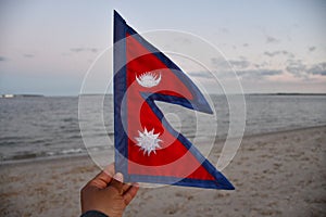 Selective focus of a hand holding the flag of Nepal on blurred sea background