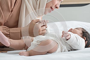 Selective focus on hand of Muslim newborn baby 1 month old grabbing young mother finger wearing hijab, lying on bed with cute