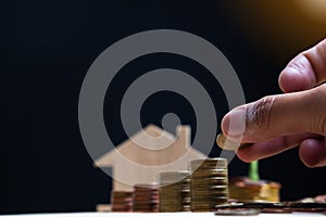 Selective focus of hand putting coins in stack with blurred house model and dark background, Planning real estate and property