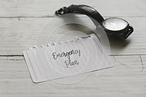 Selective focus of hand watch and paper written with Emergency Plan on white wooden background