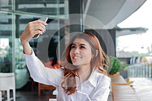 Selective focus on hands of attractive young Asian woman taking photo or selfie on mobile smart phone in office. Shallow depth of