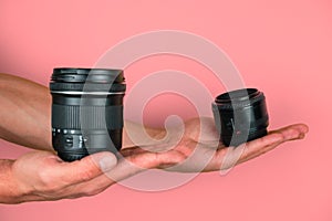 selective focus hands hold camera lenses on a pink background, comparison and choice of professional optics concept