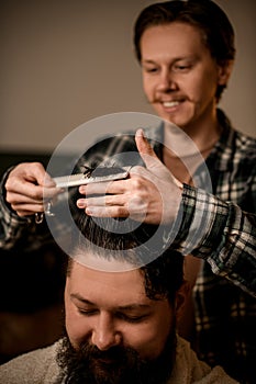 Selective focus on hands of professional barber cutting and styling hair with comb to his client