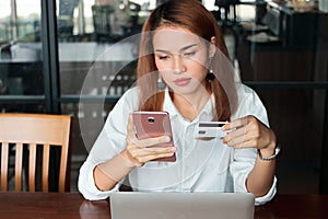 Selective focus on hands of young Asian woman holding credit card and mobile smart phone in living room. Online shopping concept.