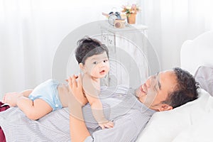 Selective focus happy father playing with 1-2 months newborn baby with love on bed at home, Asian dad and adorable infant have fun