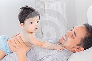 Selective focus happy father playing with 1-2 months newborn baby with love on bed at home, Asian dad and adorable infant have fun