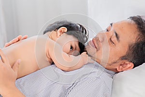 Selective focus Healthy asian father lying on bed with newborn baby. Adorable infant lying on daddy chest with safe and love. Dad