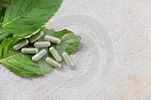 Selective focus at Herbal medicine in capsule on brown wood surface, with green  holy basil leaf herb at the background.