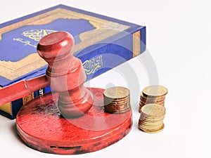 Selective focus Holy Quran written arabic calligraphy meaning of Al Quran with gavel and coins isolated on white background.