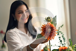 A beautiful Asian woman arranging a vase with beautiful fresh flowers at home