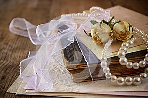 Selective focus image of dry roses, white pearls necklace and old vintage books on wooden table. retro filtered image