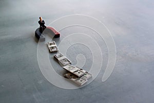 Selective focus image of miniature businessman attracts money using magnet