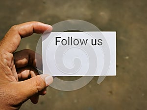 Selective focus image with noise effect hand holding white card with text FOLLOW US.