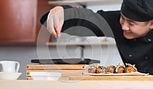 Selective focus on japanese food called takoyaki in plate from hot pan on table. Asian young chef man, in black uniform, cooking