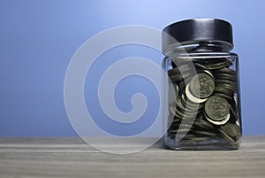 Selective focus jar full with gold coins and copy space on wooden table with a blue background