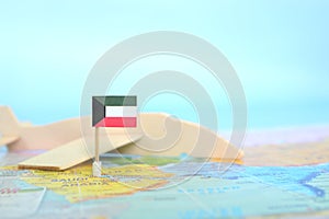 Selective focus of Kuwait flag in blurry world map and wooden airplane model. Kuwait as travel and tourism destination concept.