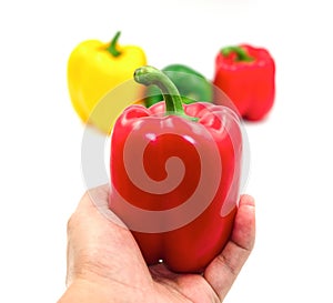 Selective focus left human hand holding fresh red and group green yellow red sweet peeper or bell pepper vegetable background. Iso