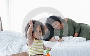 Selective focus of little African girl playing toys while mother feeding milk from bottle to her brother infant sleeping on bed