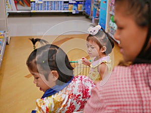 Selective focus of little Asian baby girl  furthest  looking and standing in a shopping cart with her sister photo