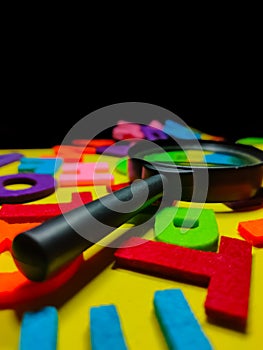 Selective focus.Magnifying glass and colorful word on black background.Education concept.Shot were noise and film grain.