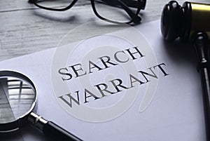 Selective focus of magnifying glass,gavel,glasses and paper written with Search Warrant on white wooden background