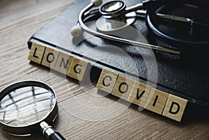 Selective focus of magnifying glass, notebook, stethoscope and wooden block written with Long Covid